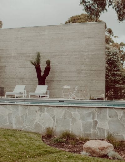 Photo of pool area with white wall, crazy paving and sun lounges