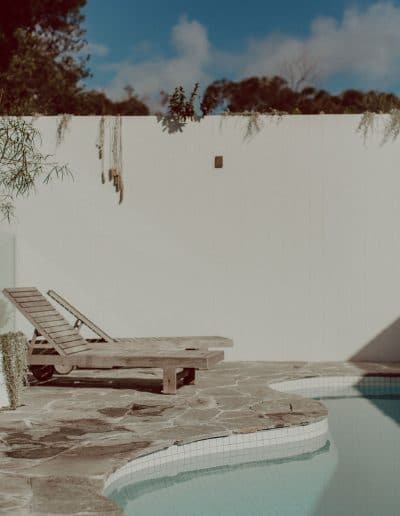 Photo of pool area with white wall, crazy paving and sun lounges